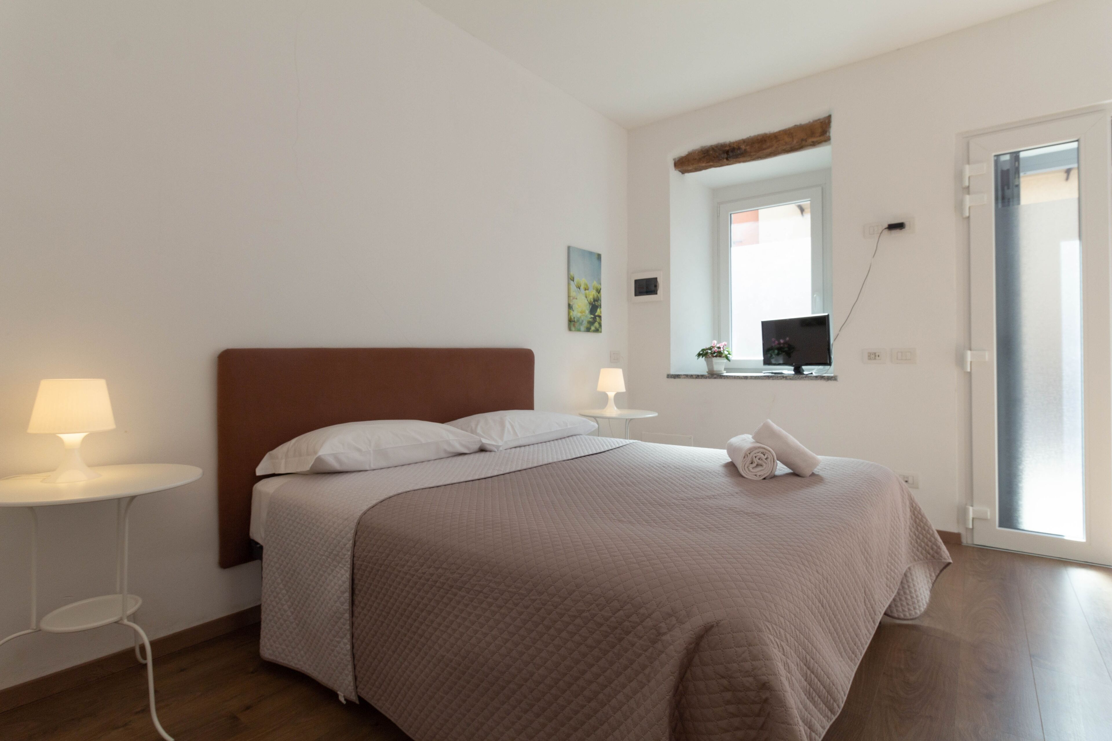 A neatly arranged bedroom with a bed, bedside lamps, a small table, and a window with a view.