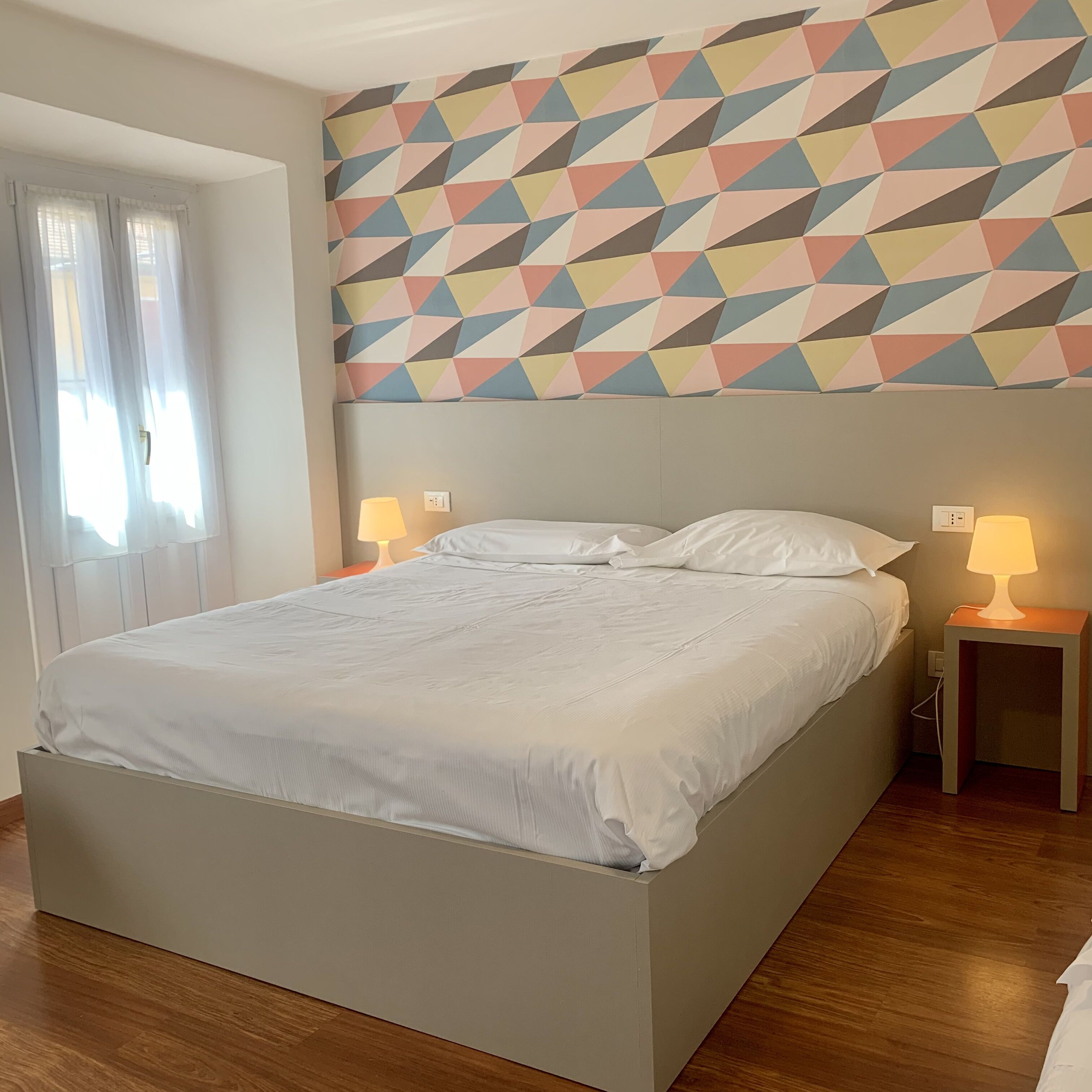 A neatly made bed in a room with a geometric-patterned wall above it.