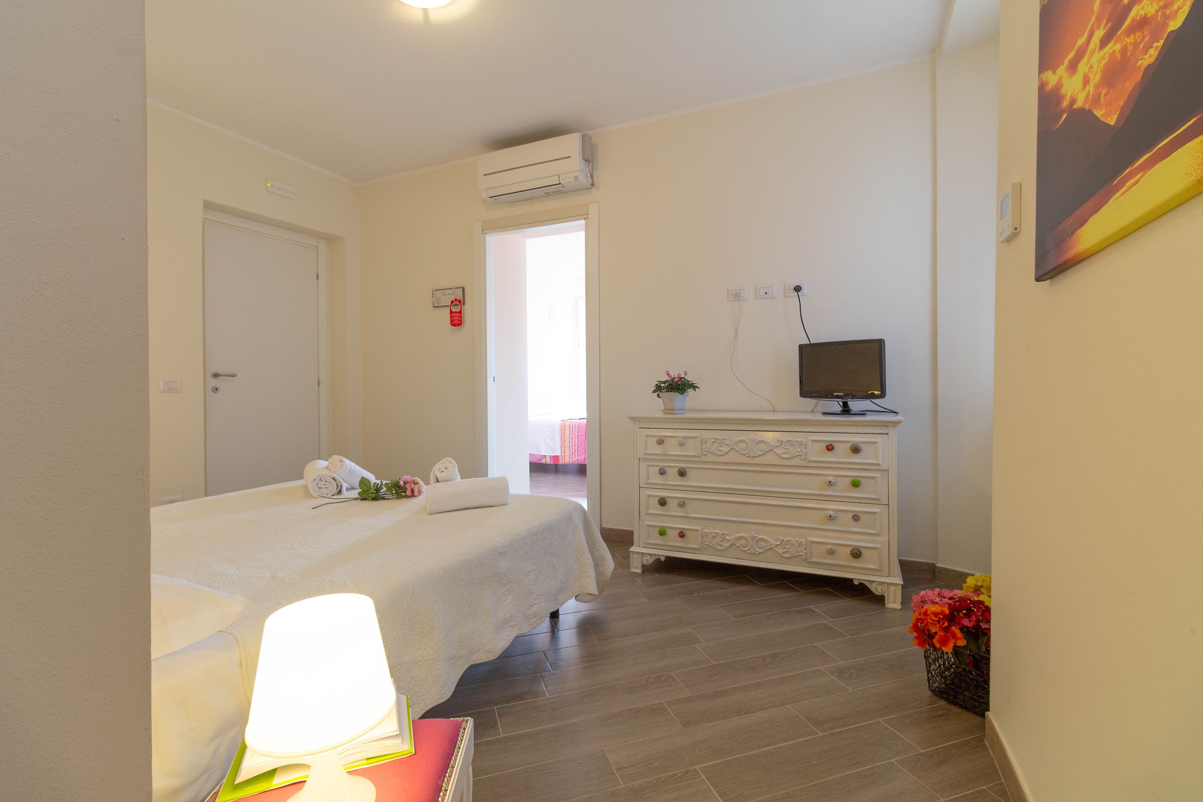 A hotel room with a bed, a dresser, a television, and a wall-mounted air conditioner.