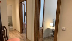 Un pasillo con puertas de madera, una silla y una mesita con lámpara.