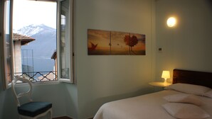 Un dormitorio con cama, una silla, una ventana con vistas a montañas y un cuadro colgado en la pared.
