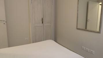 Een slaapkamer met een enkel bed, een kledingkast en een spiegel aan de muur.