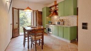 A kitchen with green cabinets, a wooden dining table, and a hanging light fixture. - Donna Nobile (San Gimignano)