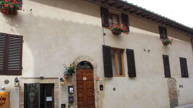 A building with a wooden door, windows with shutters, and flower boxes. - Donna Nobile (San Gimignano)