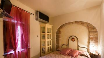 A bedroom with a bed, a TV mounted on the wall, a wardrobe, and a stone archway.