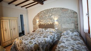 A bedroom with two beds, a wardrobe, and a stone wall arch. - Donna Nobile (San Gimignano)