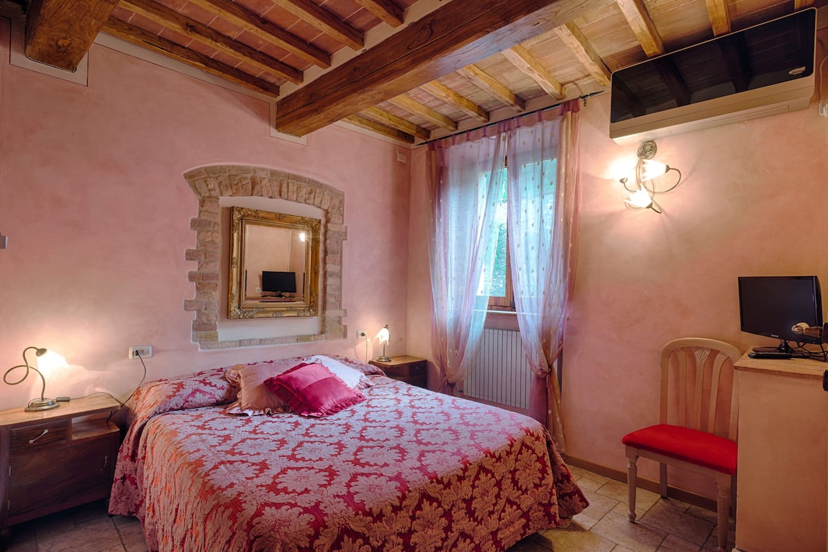 A bedroom with a bed, a wooden desk, a chair, a mirror, and a television.