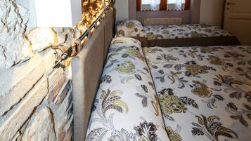 A bedroom with a stone wall, a bed with patterned bedding, a window with curtains, and a wooden door.