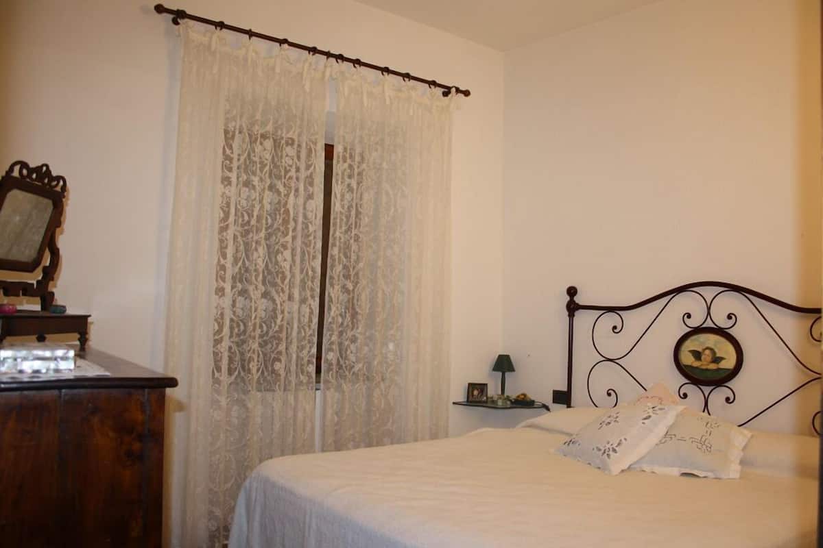 A bedroom with a bed, a wooden dresser, a nightstand with a lamp, and a decorative headboard.
