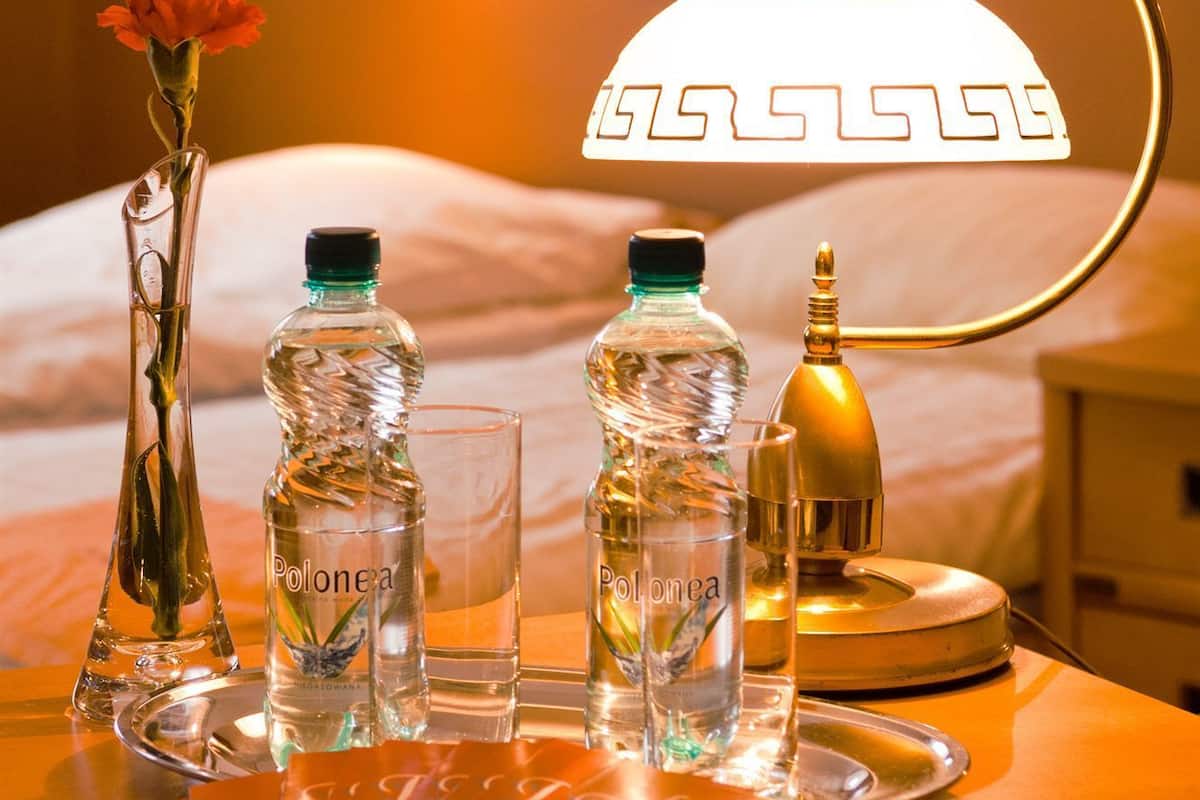 A hotel room with a bed, a bedside lamp, and a tray with bottles and a glass.