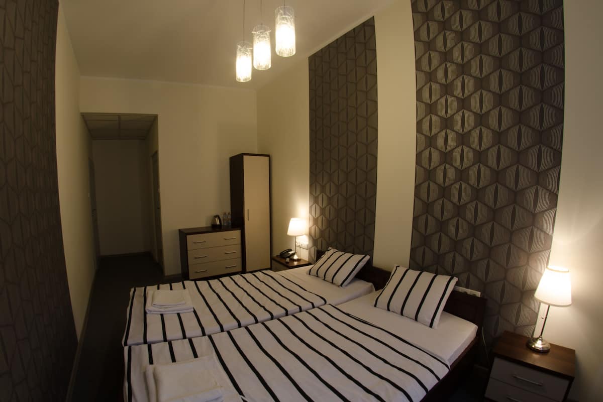A hotel room with a large bed, two bedside tables, a wardrobe, and a patterned wall.