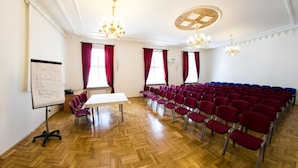 Una sala conferenze con pavimento in legno, una lavagna, un tavolo e file di sedie rosse e blu.