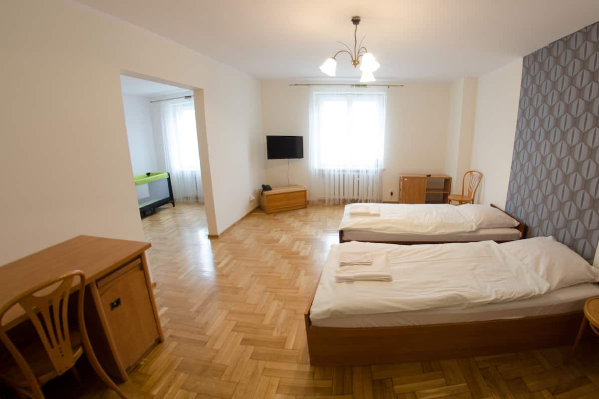 A hotel room with two beds, a desk, a chair, a TV, and a window with curtains.