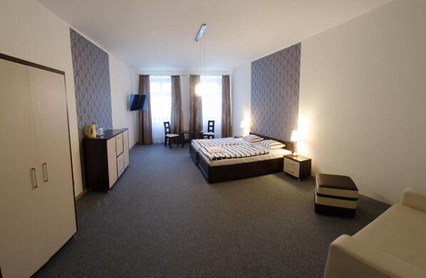 A hotel room with a bed, a desk with a chair, a TV, and a wardrobe.