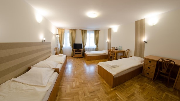 Una camera d'albergo con due letti singoli, un letto matrimoniale, una TV, un tavolino con sedie e una scrivania con una sedia.