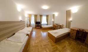 Hotellihuone, jossa on kaksi erillistä sänkyä, yksi parivuode, televisio, pieni pöytä tuoleineen sekä työpöytä tuolilla.