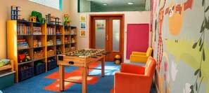 A children's playroom with a foosball table, shelves with toys and books, and a colorful mural.