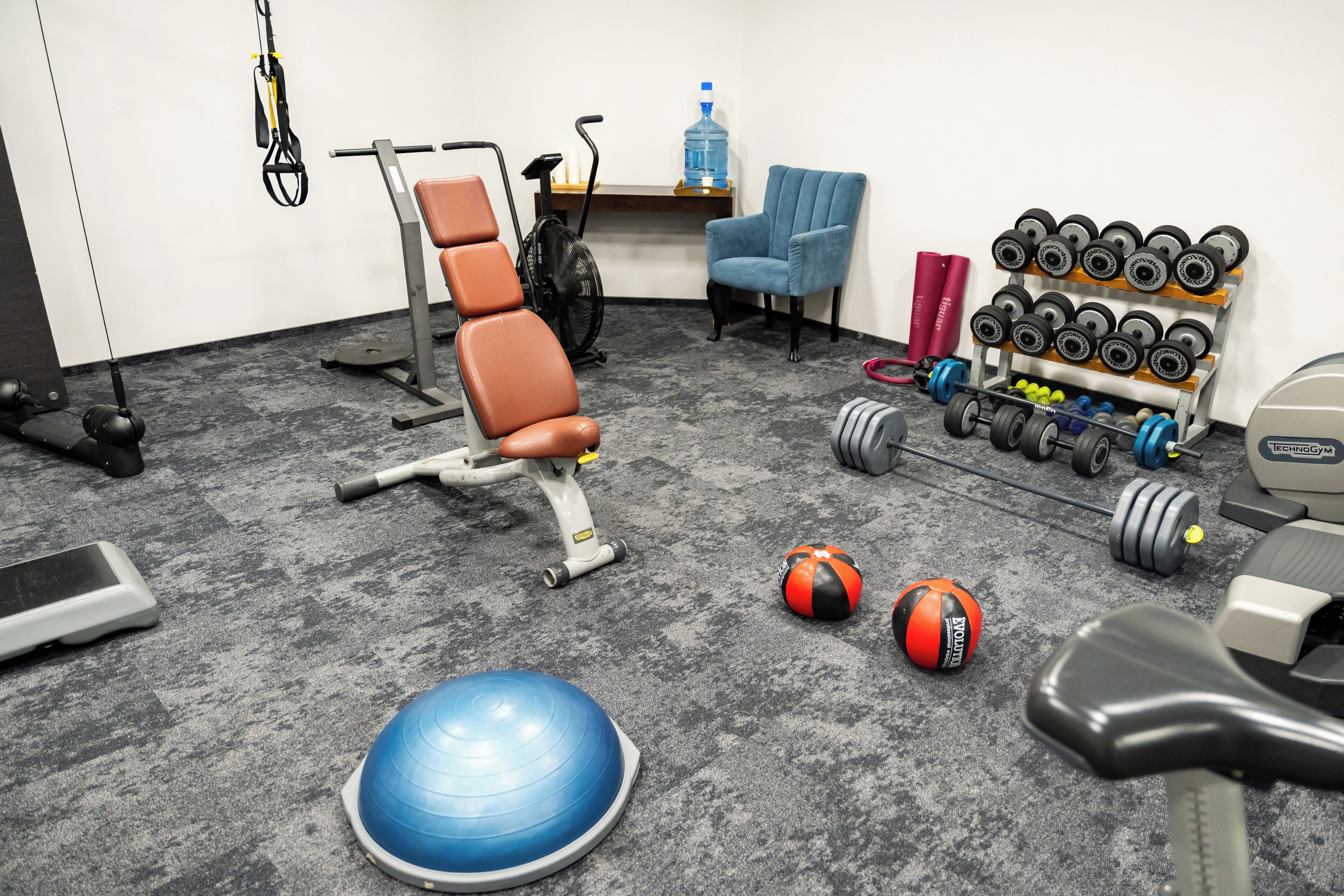 Une salle de sport équipée de matériel d’exercice, une chaise bleue et un distributeur d’eau.
