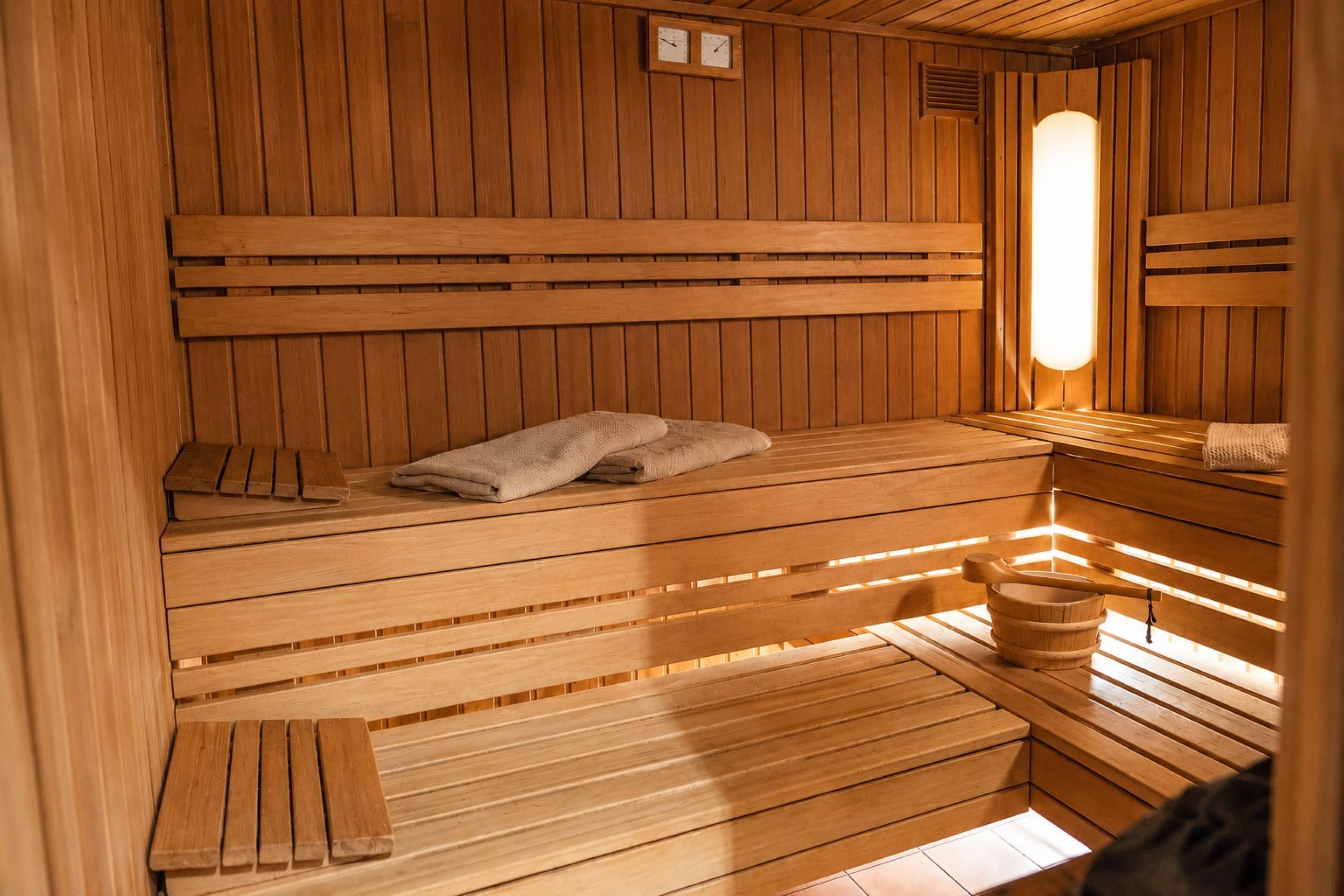 Un sauna avec des bancs en bois, un banc avec des serviettes et un seau en bois.