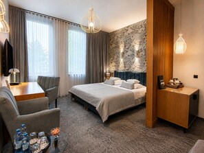 A hotel room with a bed, a desk, a chair, a TV, and a coffee station.