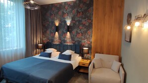 Habitación de hotel con una cama grande, una silla, una mesita de noche y una pared con estampado floral.