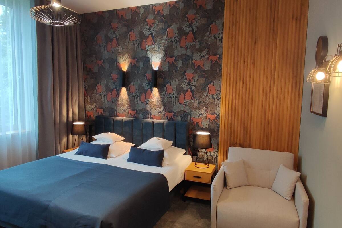 Habitación de hotel con una cama grande, una silla, una mesita de noche y una pared con estampado floral.