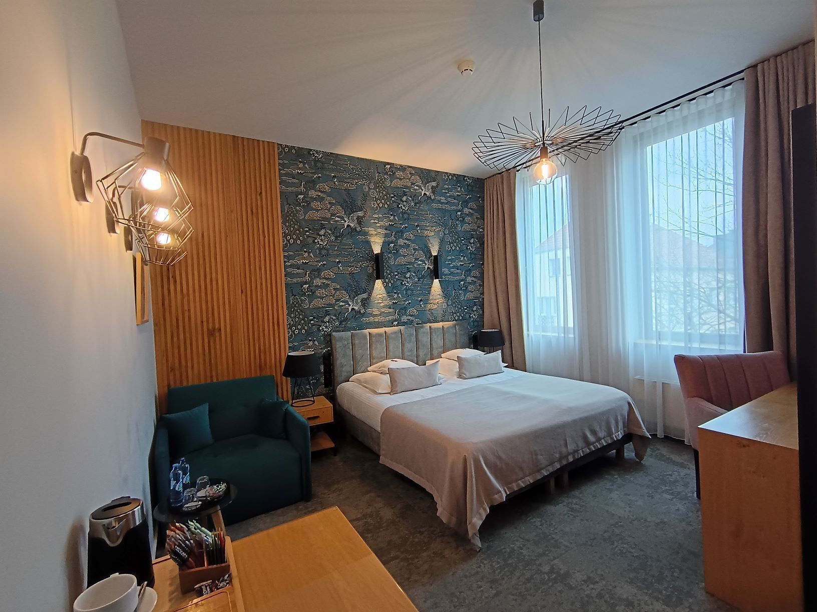 Ein Hotelzimmer mit Bett, Schreibtisch, Stuhl, einer Kaffeemaschine und einer Wand mit dekorativem Muster.