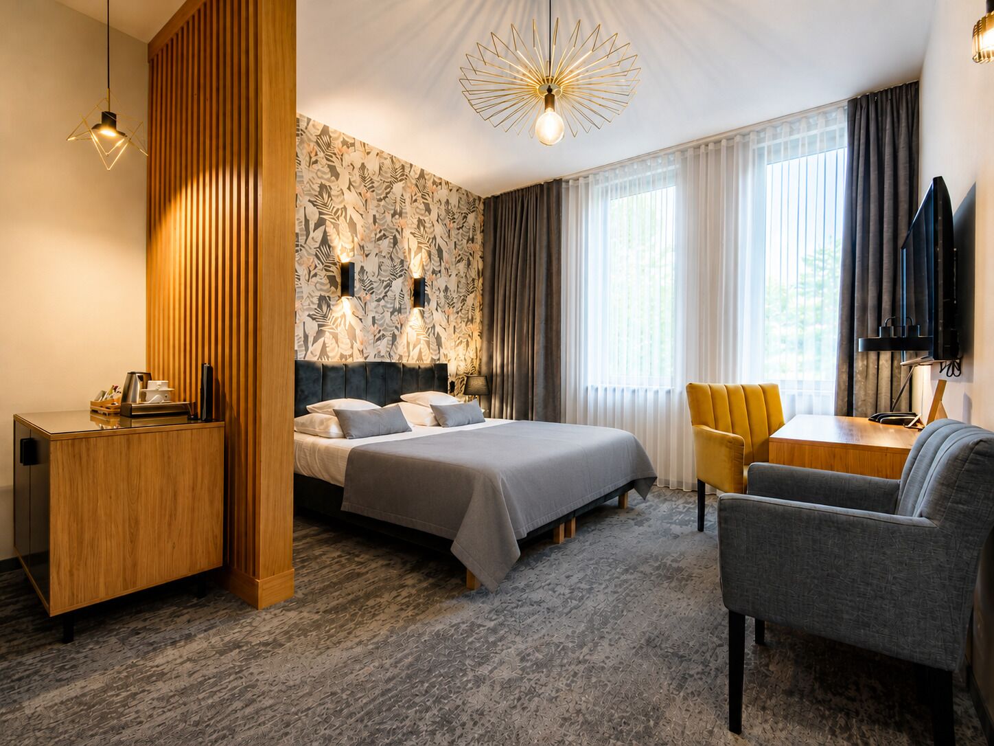 A hotel room with a bed, a desk, a chair, a TV, and a large window with curtains.