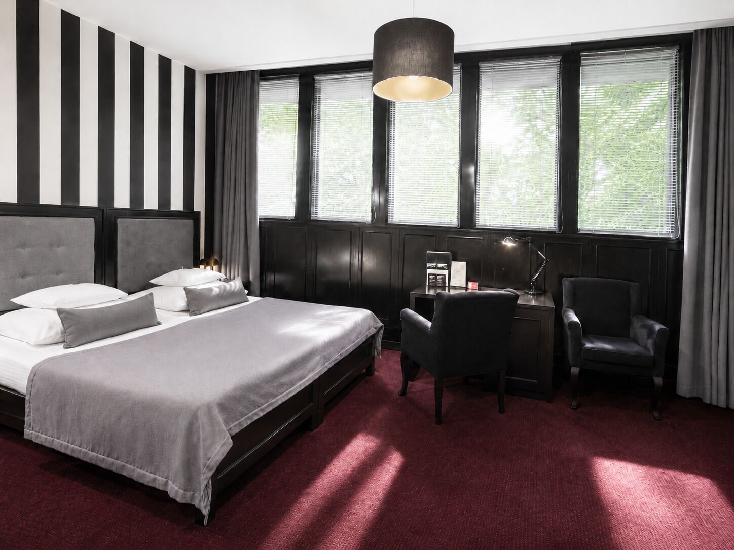 Habitación de hotel con una cama grande, un escritorio con una silla y una ventana con persianas.