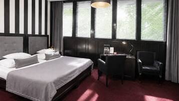 Habitación de hotel con una cama grande, un escritorio con una silla y una ventana con persianas.