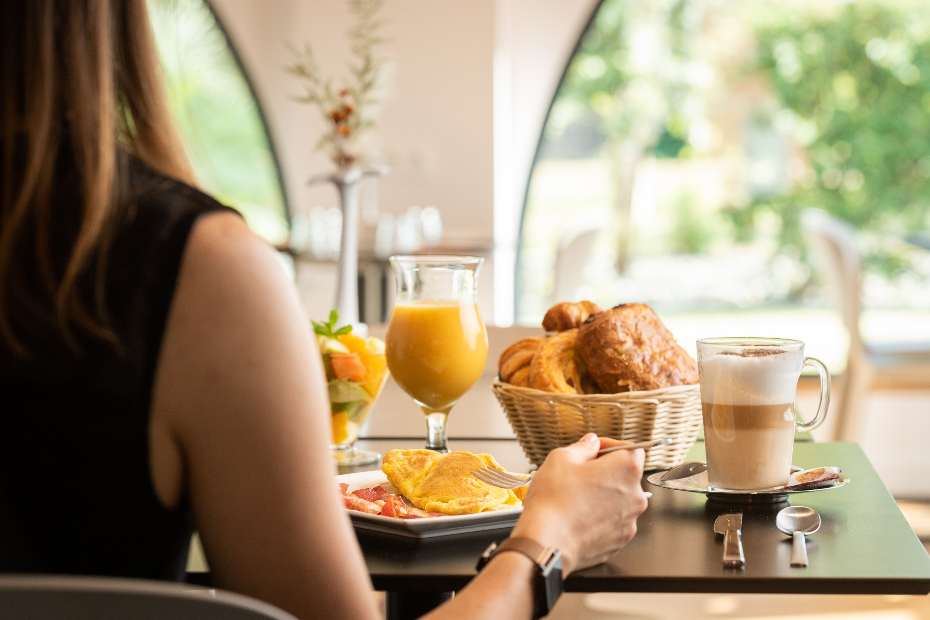 A breakfast setting with a table, a basket of croissants, a glass of orange juice, and a cup of coffee.