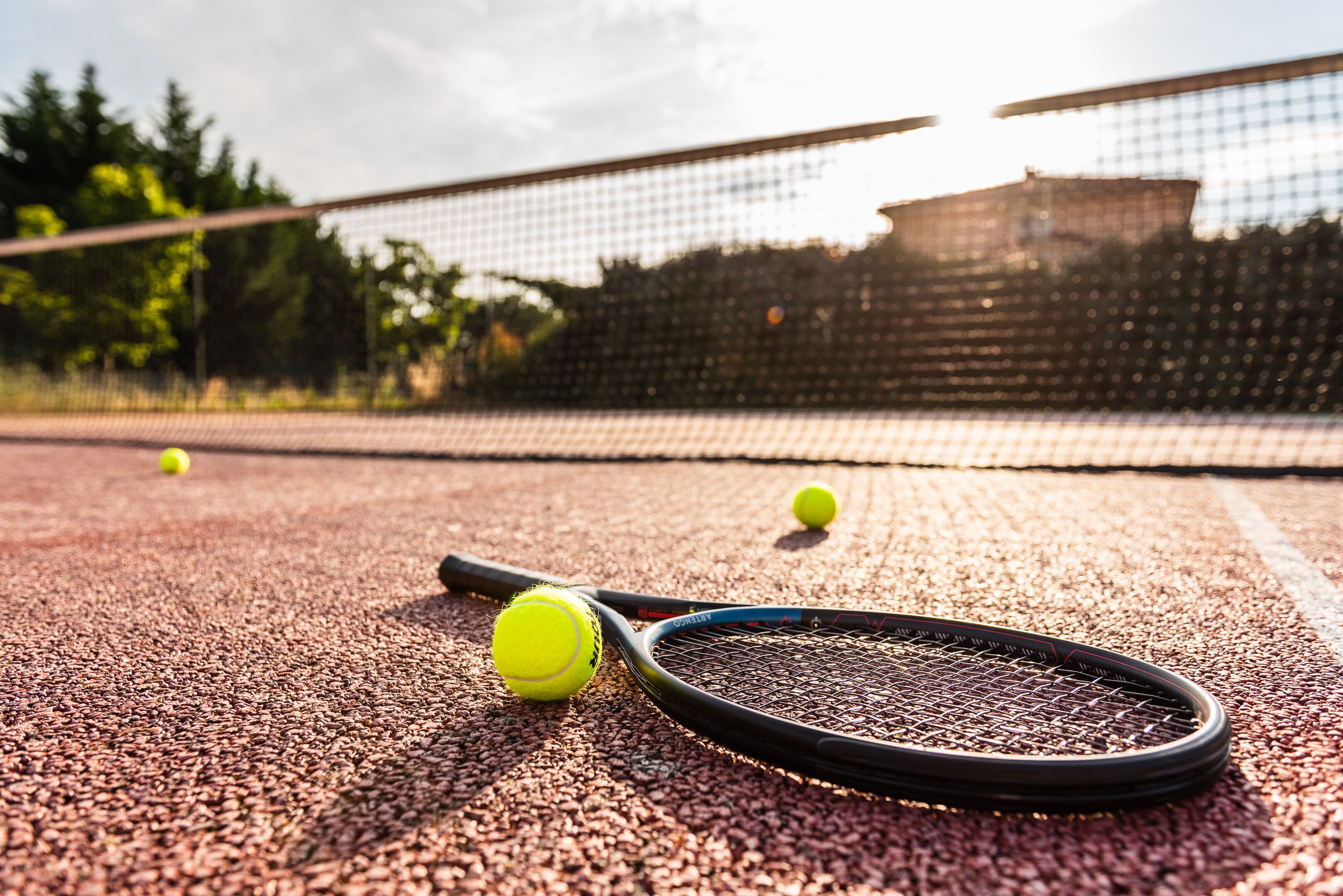 A tennis court with a net, two tennis balls, and a racket.