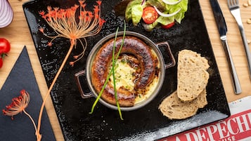 A meal with sausages, bread, and a salad on a black plate.