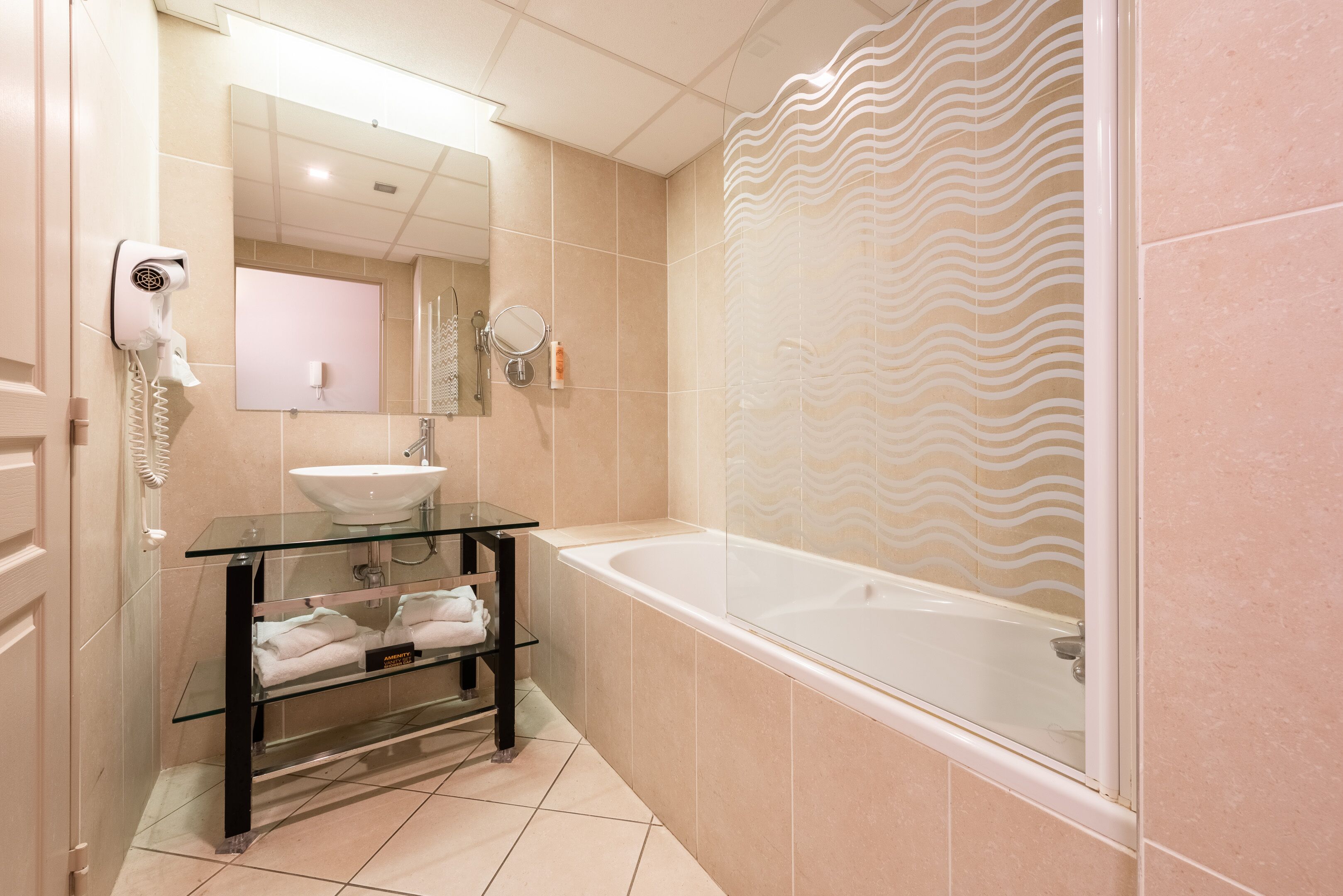 A modern bathroom with a glass shelf holding towels, a sink, and a hairdryer.