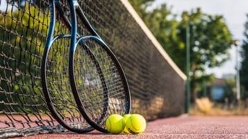 A tennis court with two tennis rackets leaning against the net and three tennis balls on the ground.