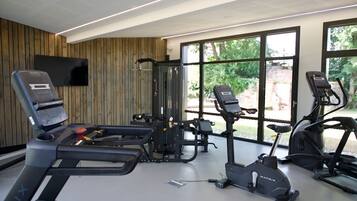 Ett modernt gym med konditionsmaskiner, styrketräningsutrustning och stora fönster med utsikt över grönområden.