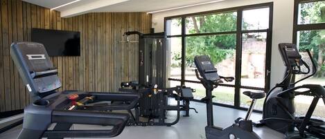 Et moderne fitnesscenter med løbebånd, styrketræningsudstyr og store vinduer med udsigt til grønne områder.