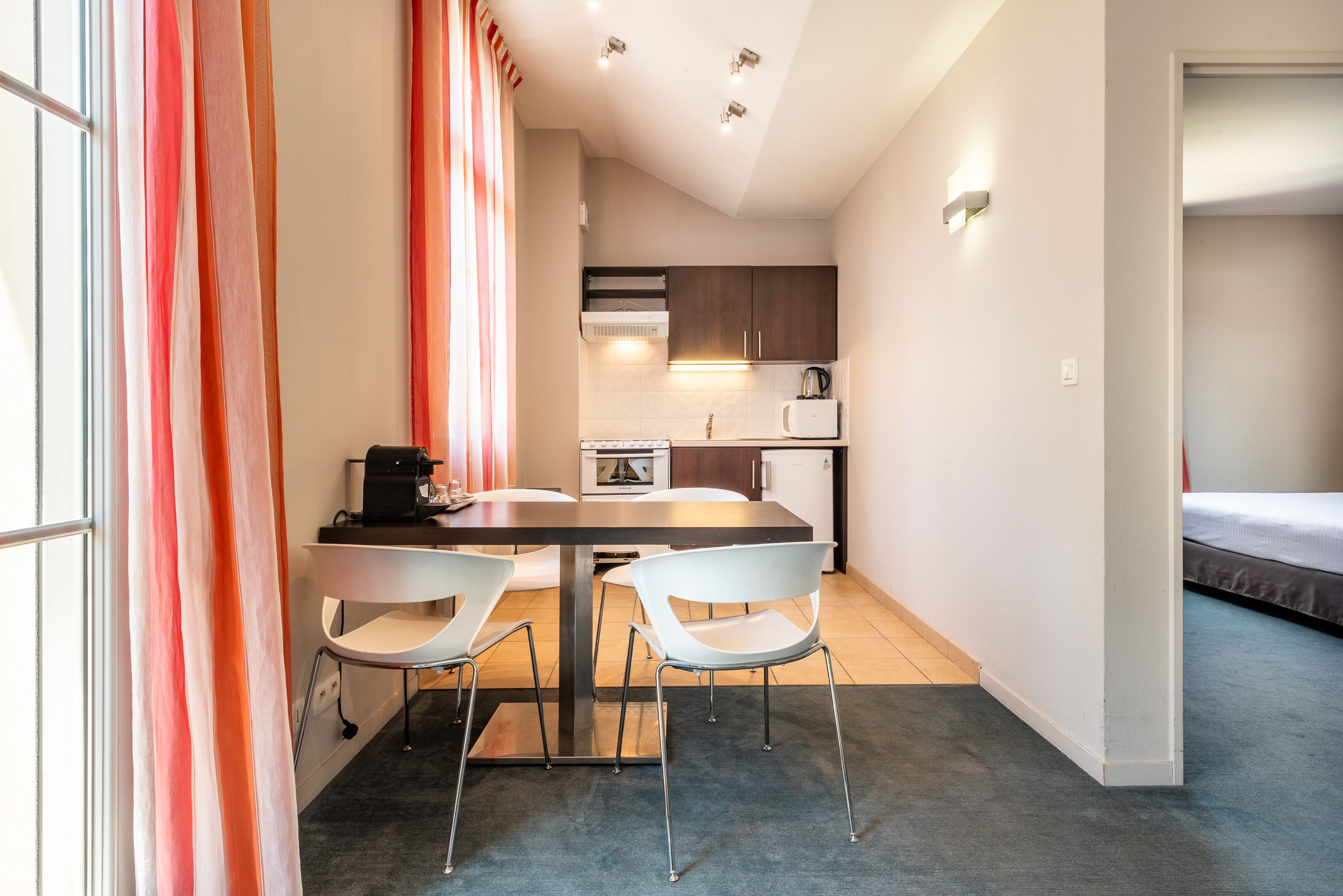 Una cocina compacta con electrodomésticos modernos, un comedor con dos sillas y una cama en la habitación contigua.