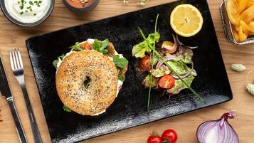 A black plate with a bagel sandwich and a salad on a wooden table.
