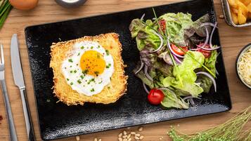 Une assiette noire sur laquelle repose un œuf au plat, posé sur une base croustillante, accompagnée d’une salade et d’un bol de soupe.