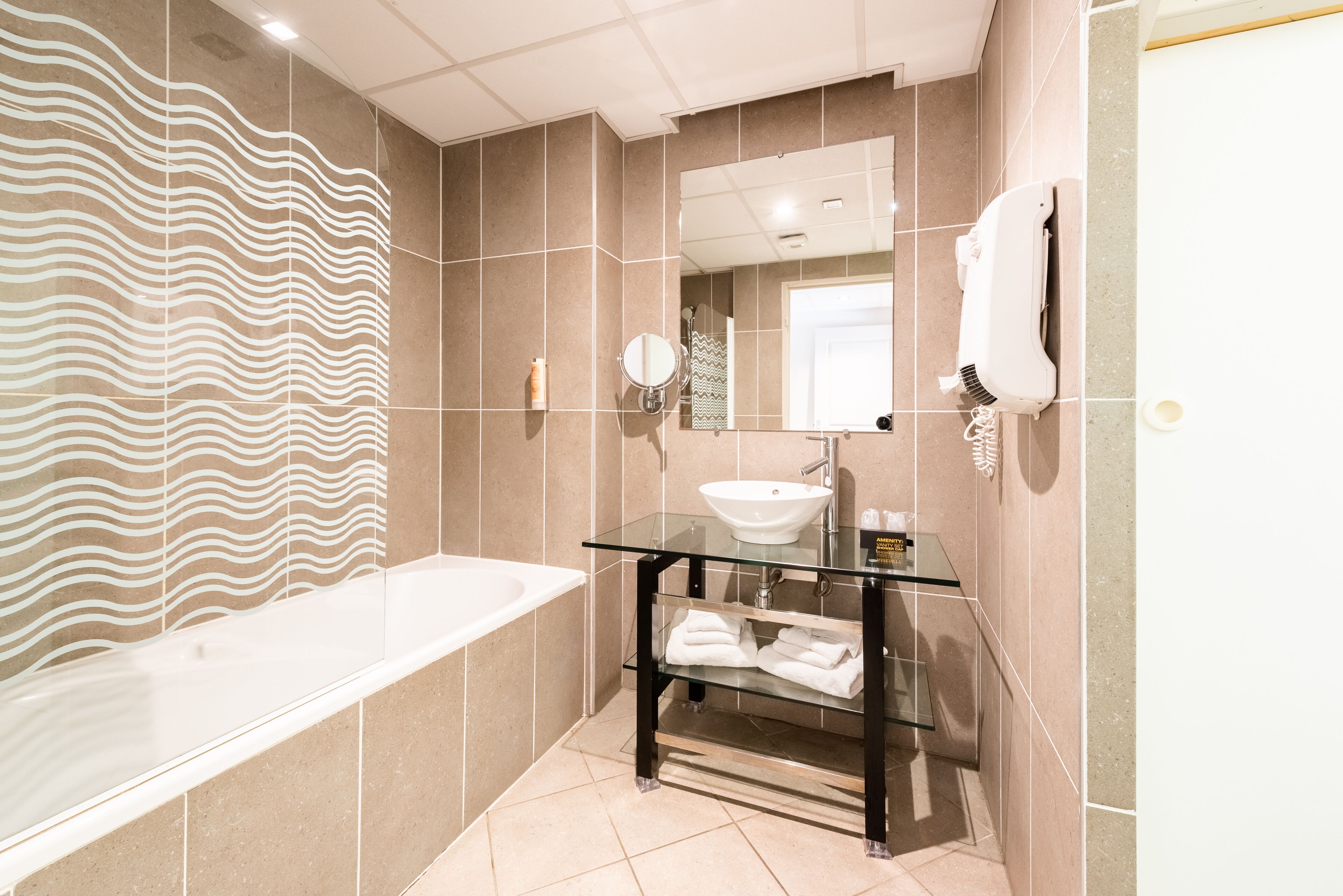 A modern bathroom with a glass-enclosed vanity, a white sink, and a large bathtub.