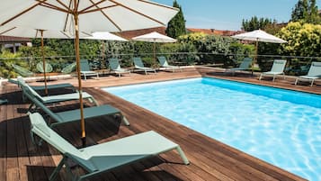 A wooden deck with a swimming pool, lounge chairs, and umbrellas.