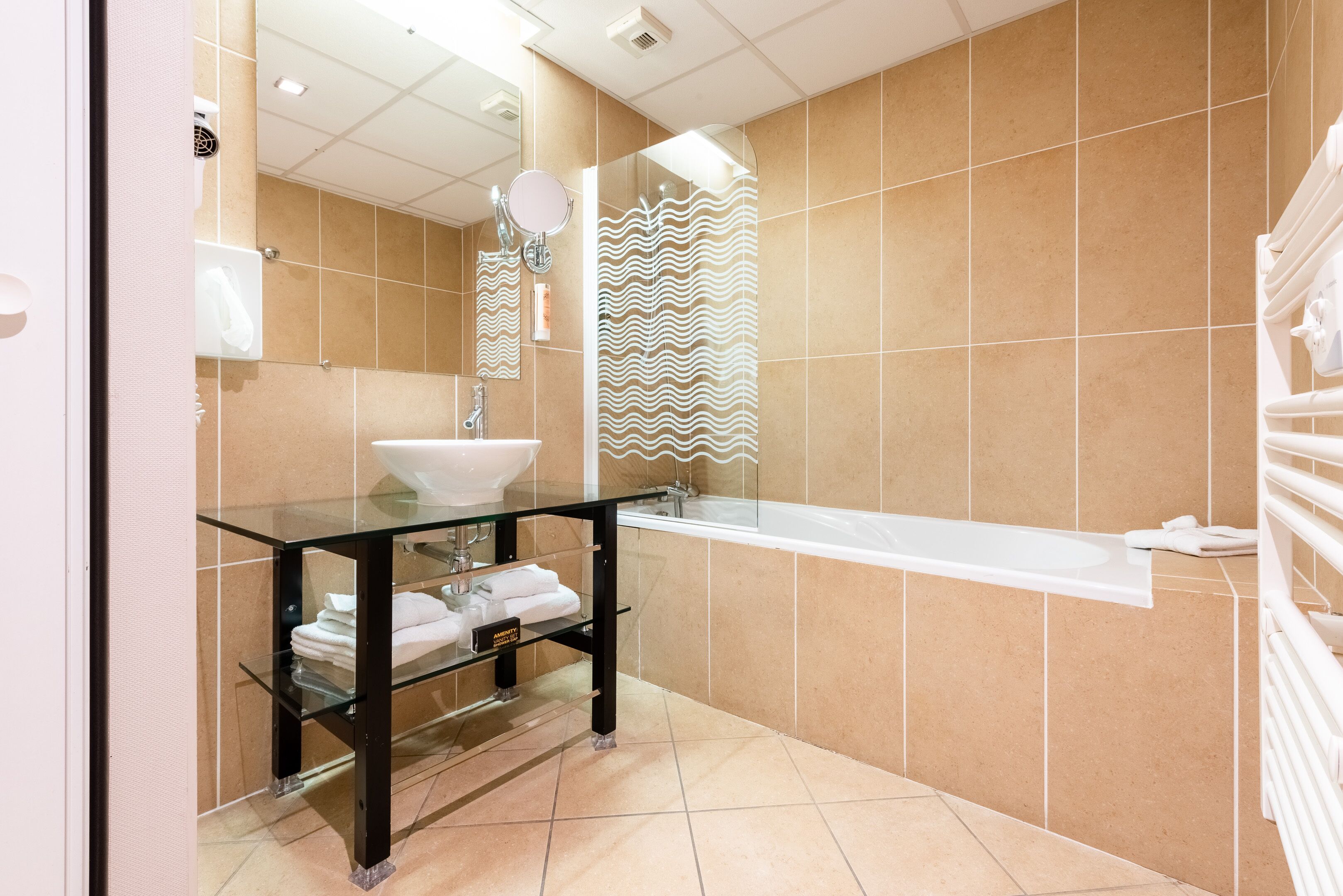 Une salle de bain moderne avec un lavabo en verre, une baignoire blanche et des carreaux de couleur beige.