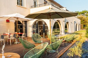 An outdoor patio with wooden flooring, green wireframe chairs, and white umbrellas. - Residence de Diane (Toulouse)