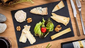 A cheese board with various cheeses, walnuts, and a cherry tomato on a slate board.