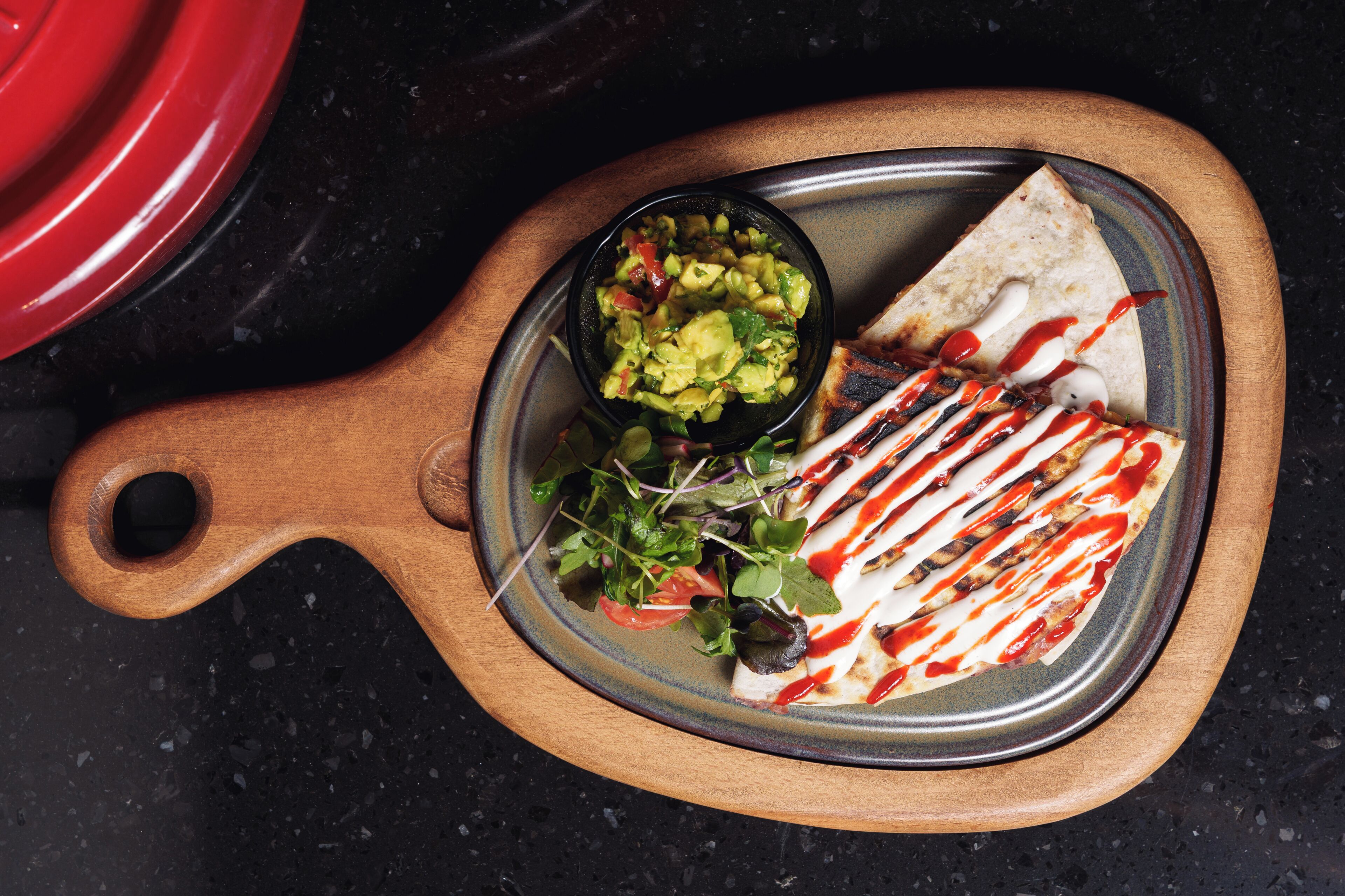 Een houten serveerplank met een tortilla wrap, een kommetje guacamole en een salade.