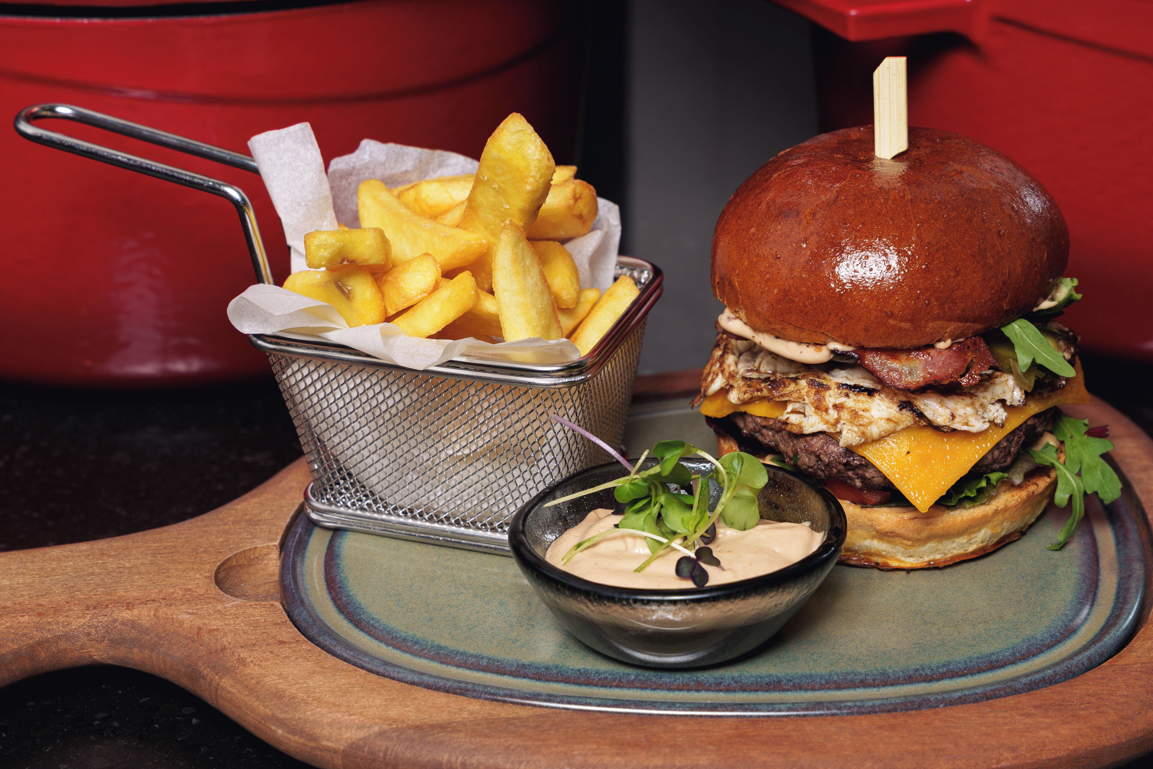 En burger med pommes frites og en lille skål med sauce på en træplade.
