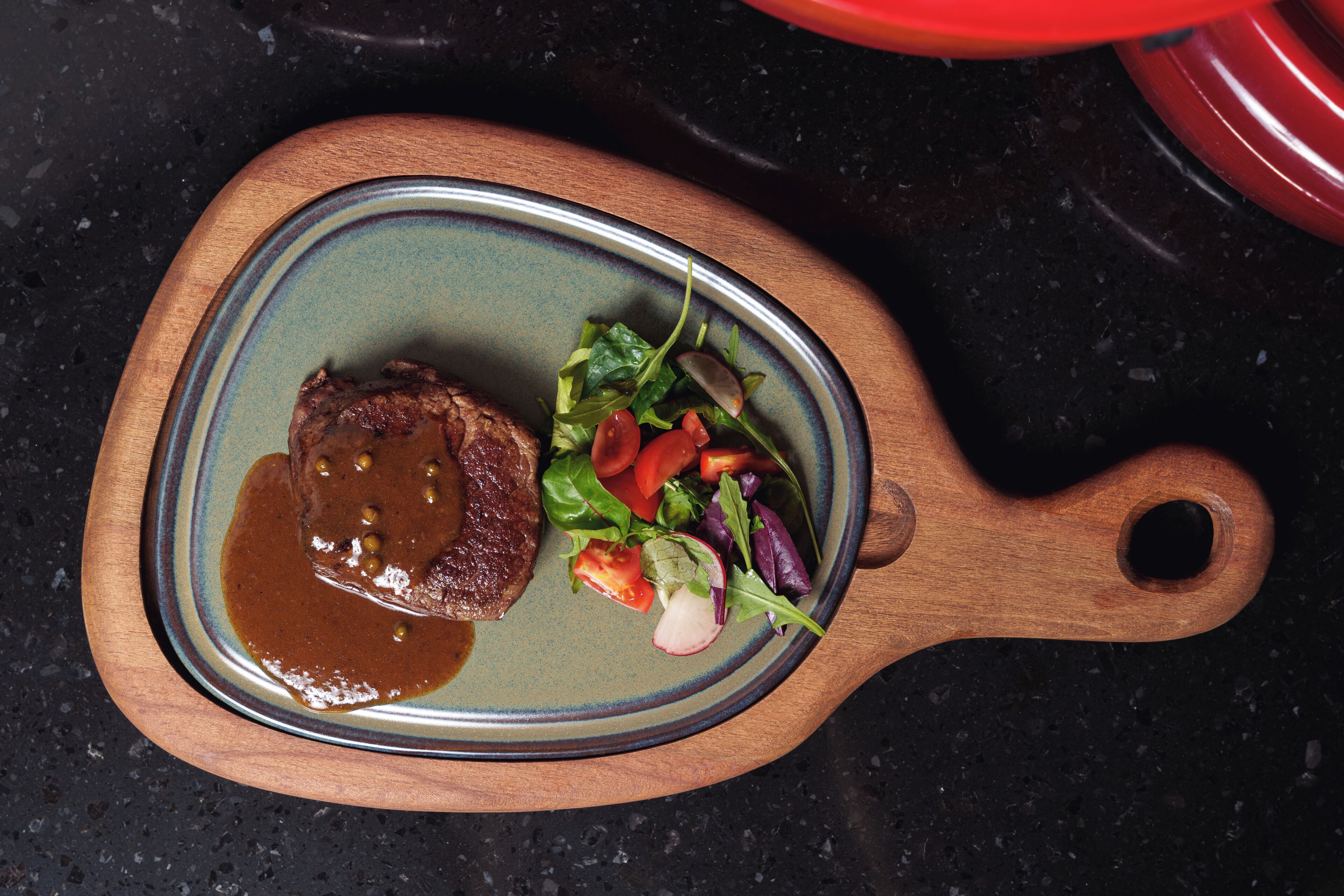 Un plato con bistec y ensalada sobre una tabla de madera.