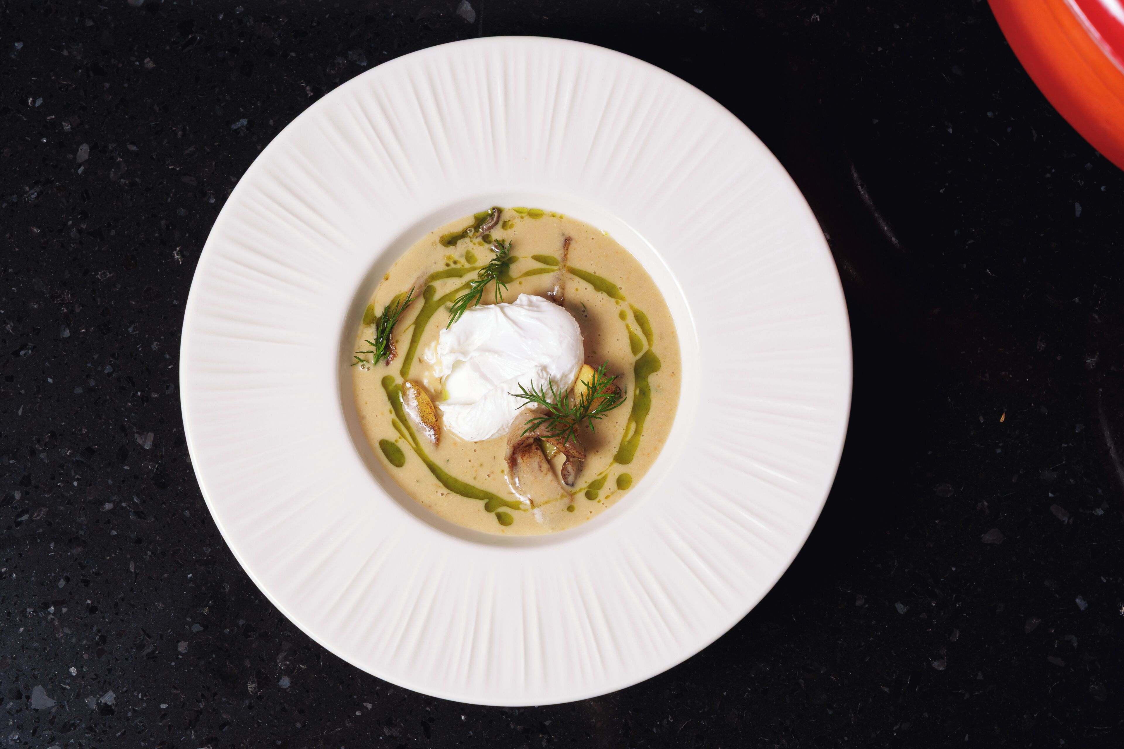 A white plate with a creamy dish, garnished with dill and green sauce, on a dark surface.