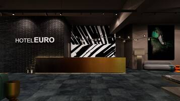 A modern hotel reception area with a black brick wall, a reception desk, and a large abstract painting.